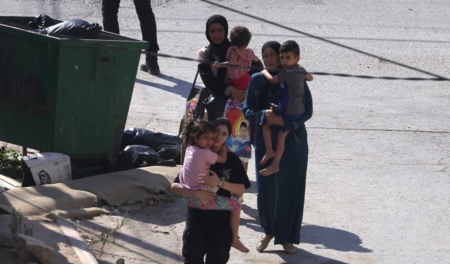 palestinos, entre ellos mujeres y niños, pasan junto a las tropas israelíes cuando abandonan el campo de refugiados de Jenin