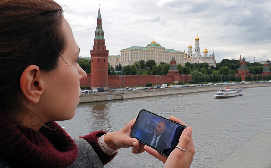 Una mujer mira su teléfono inteligente que muestra al presidente ruso Vladimir Putin hablando