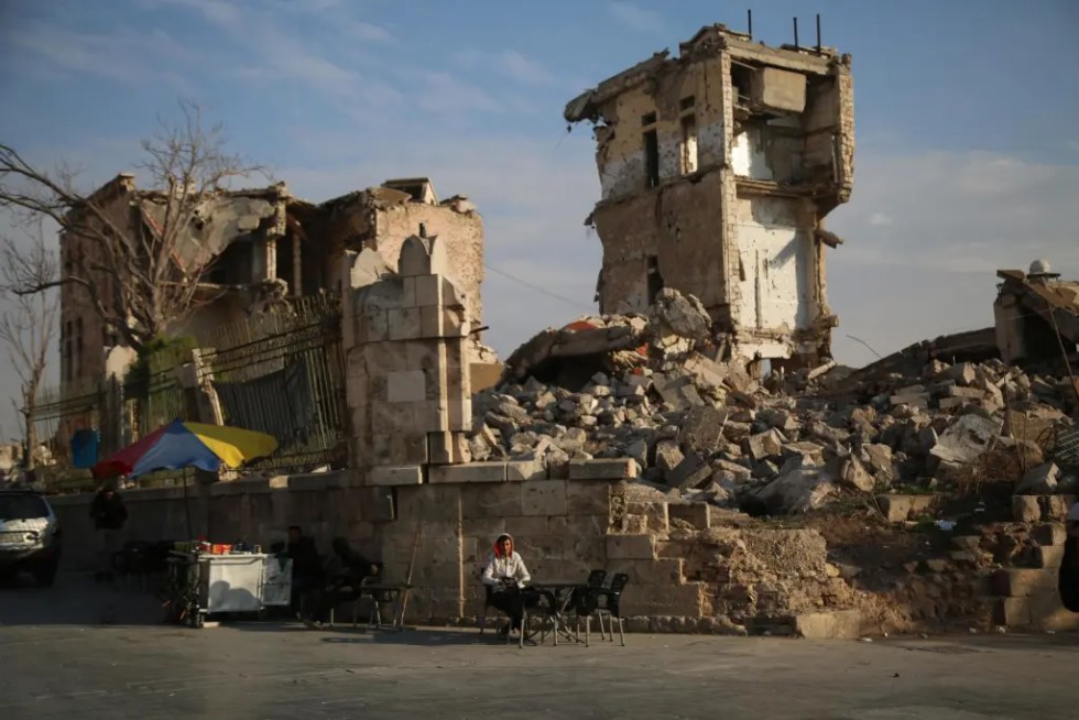 Un vendedor ambulante sentado frente a un edificio dañado en Alepo, Siria.