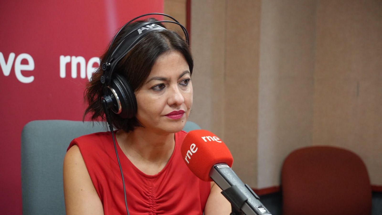 Sira Rego: "Hacer politiqueo con los derechos de la infancia no es ser solidario" Sira Rego, con auriculares AKG y blusa roja, en un estudio de RNE con micrófono rojo y logo visible.
