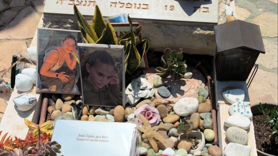 Tumba conmemorativa de Maya Villalobo en Israel, decorada con fotografías, plantas, piedras con mensajes y elementos de homenaje.