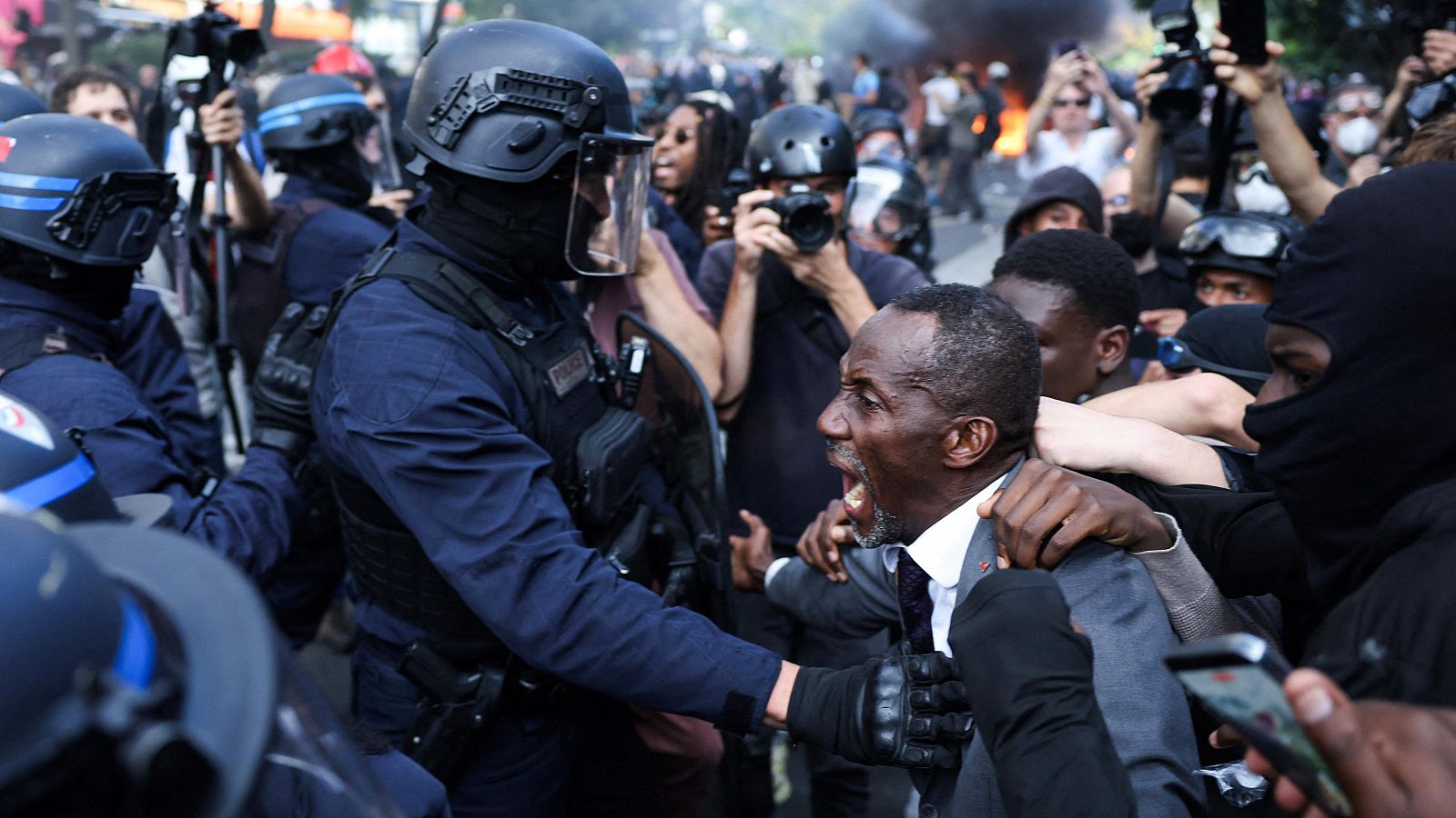 El alcalde de Saint Denis, símbolo de las protestas estudiantiles en Francia Un hombre con traje gris y barba grita en una protesta callejera mientras un policía antidisturbios intenta contenerlo con la mano en el pecho.