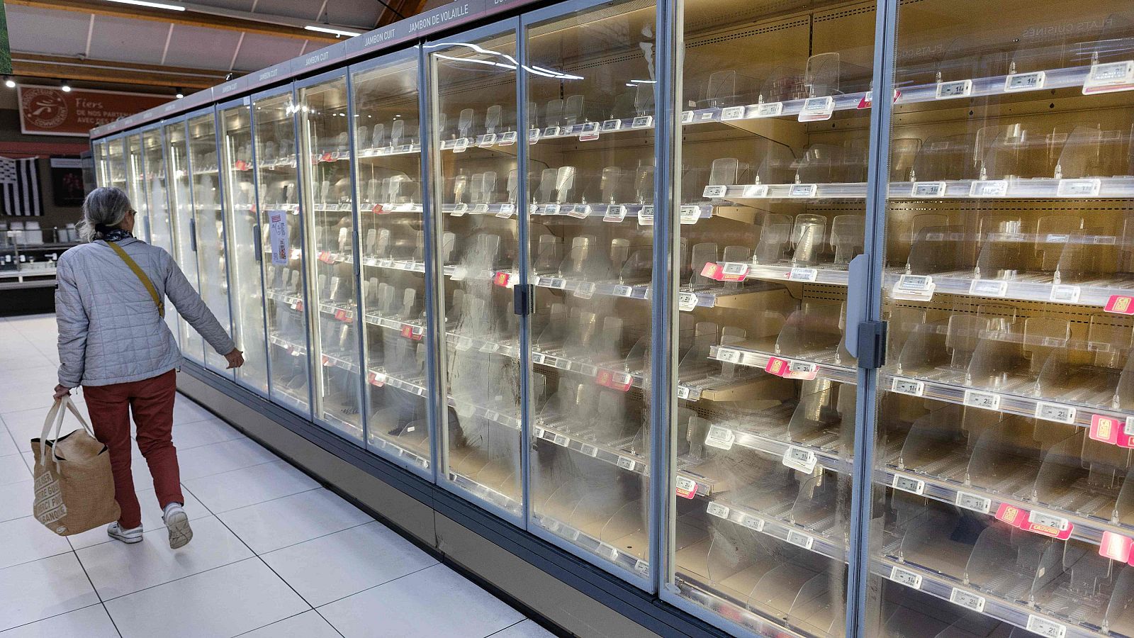 De los PIG a los FROG: Francia atraviesa una delicada crisis financiera Una mujer camina junto a refrigeradores vacíos en un supermercado con estantes desiertos y suelo brillante.